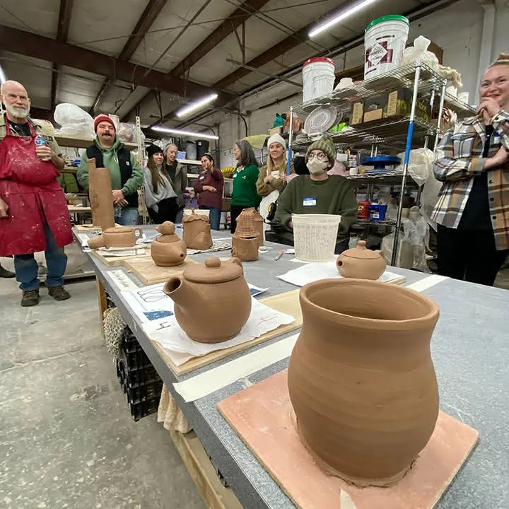 Group of people standing around a table displaying handmade pottery pieces