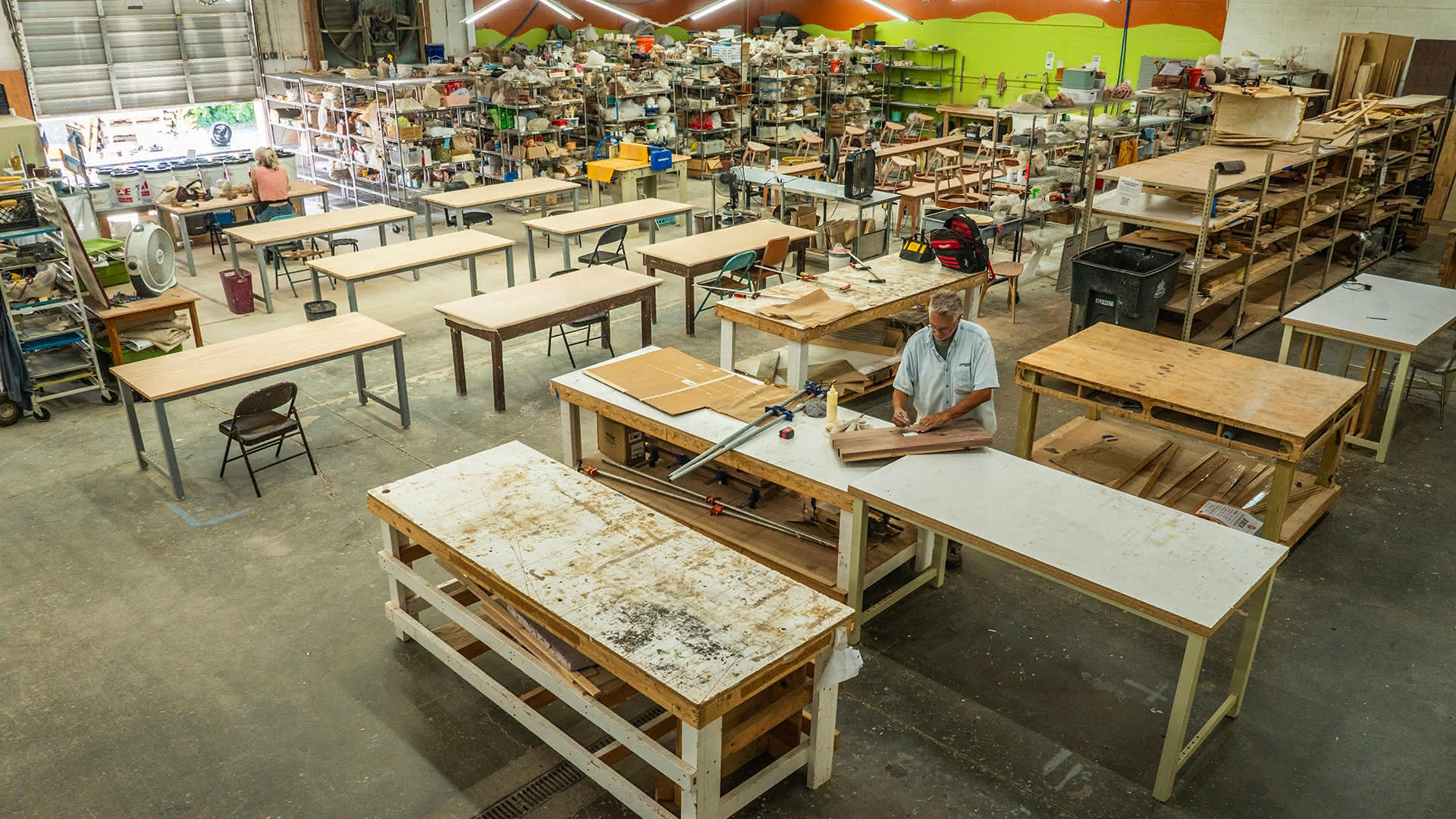 The woodshop at 620B Davidson Street, a long row of workbenches in a large open warehouse with a member working at one of the benches.